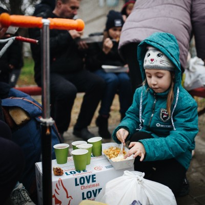 A young Ukrainian girl eats a hot meal outside in her war-torn town